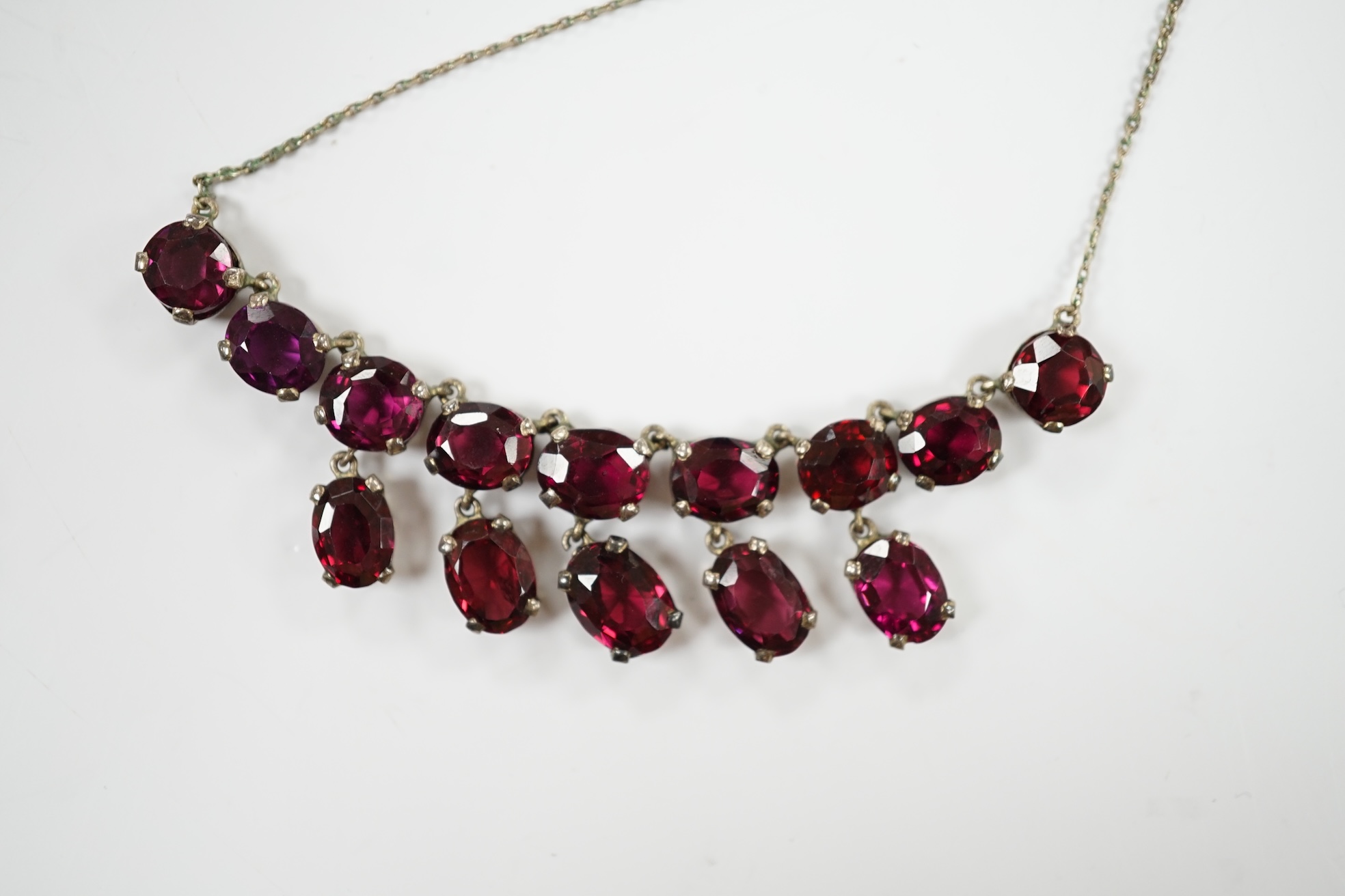 A white metal and garnet cluster set drop necklace, overall 48cm, together with a white metal, sapphire? and diamond cluster set pendant, on a white metal chain. Condition - fair